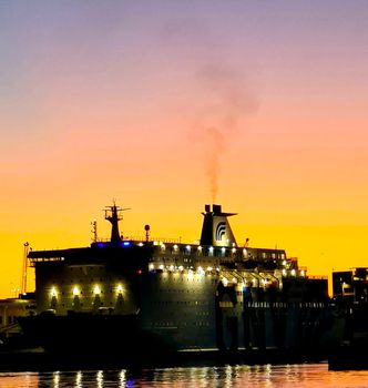 Genova, Italy - February 22, 2022: Evening view of Genoa (Genova) port, Italy with port cranes and industrial zone. Genoa, Italy. Lanterna lights by night. City illuminated behind the sea.