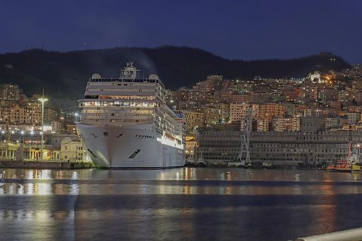 Genova, Italy - February 22, 2022: Evening view of Genoa (Genova) port, Italy with port cranes and industrial zone. Genoa, Italy. Lanterna lights by night. City illuminated behind the sea.