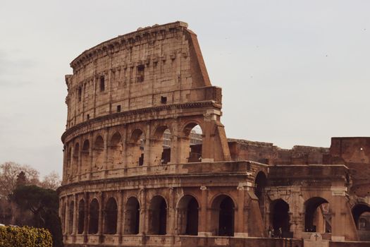 ROME, ITALY - February 05, 2022: Panoramic view around the Colosseum in city of Rome, Italy. Cold and gray sky in the background. Macro photography of the green parks with the old buildings.