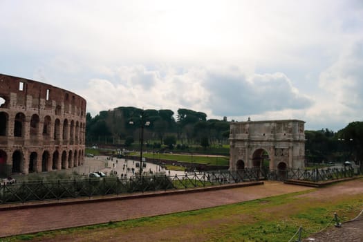 ROME, ITALY - February 05, 2022: Panoramic view around the Colosseum in city of Rome, Italy. Cold and gray sky in the background. Macro photography of the green parks with the old buildings.