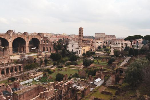 ROME, ITALY - February 05, 2022: Panoramic view around the Colosseum in city of Rome, Italy. Cold and gray sky in the background. Macro photography of the green parks with the old buildings.