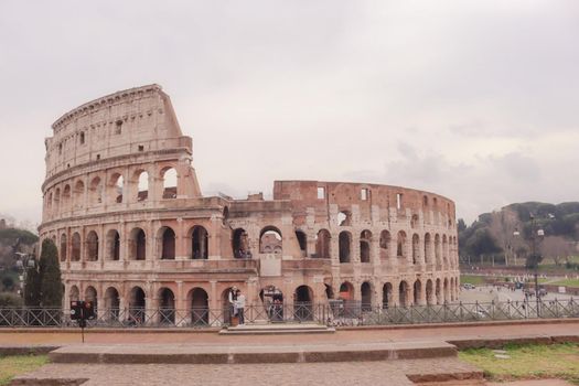 ROME, ITALY - February 05, 2022: Panoramic view around the Colosseum in city of Rome, Italy. Cold and gray sky in the background. Macro photography of the green parks with the old buildings.