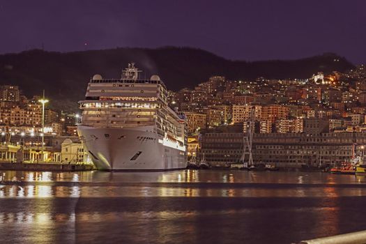 Genova, Italy - February 22, 2022: Evening view of Genoa (Genova) port, Italy with port cranes and industrial zone. Genoa, Italy. Lanterna lights by night. City illuminated behind the sea.