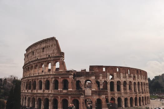 ROME, ITALY - February 05, 2022: Panoramic view around the Colosseum in city of Rome, Italy. Cold and gray sky in the background. Macro photography of the green parks with the old buildings.