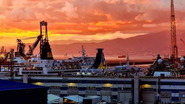 Genova, Italy - February 22, 2022: Evening view of Genoa (Genova) port, Italy with port cranes and industrial zone. Genoa, Italy. Lanterna lights by night. City illuminated behind the sea.