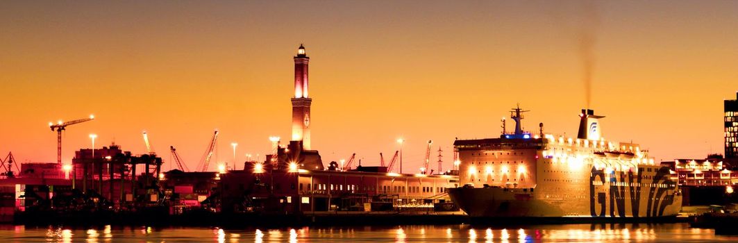 Genova, Italy - February 22, 2022: Evening view of Genoa (Genova) port, Italy with port cranes and industrial zone. Genoa, Italy. Lanterna lights by night. City illuminated behind the sea.