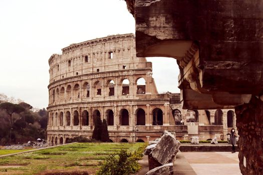 ROME, ITALY - February 05, 2022: Panoramic view around the Colosseum in city of Rome, Italy. Cold and gray sky in the background. Macro photography of the green parks with the old buildings.