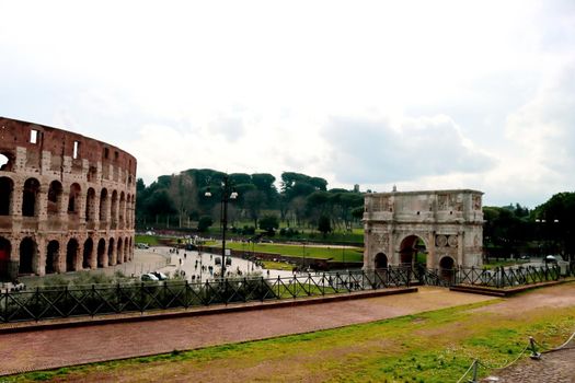 ROME, ITALY - February 05, 2022: Panoramic view around the Colosseum in city of Rome, Italy. Cold and gray sky in the background. Macro photography of the green parks with the old buildings.