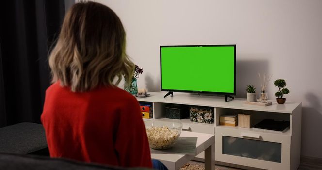 Woman watching TV focused eating popcorn. Green Screen TV Chroma Key. Movie time Sports Match, News, Sitcom TV Show in the evening.