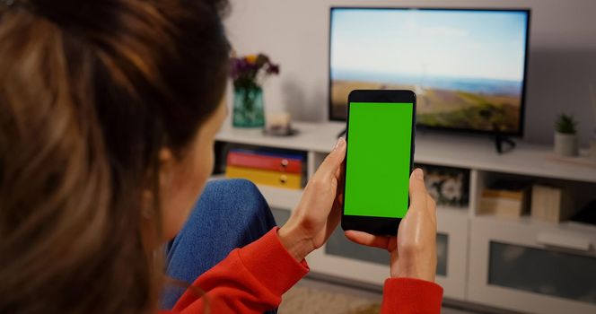 Close-up shot of green screen template smartphone in female hands at home, girl is watcing content without touching gadget screen. Modent technology and information concept.