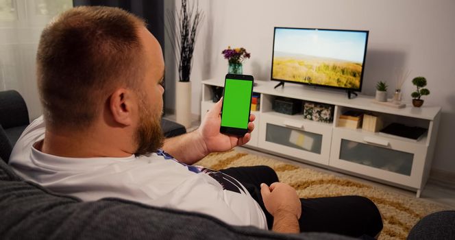 Man Using Smartphone with Green Screen for Copy Space Chroma Key Mockup. Scrolling Gestures. Male watching gadget green screen and touch display.