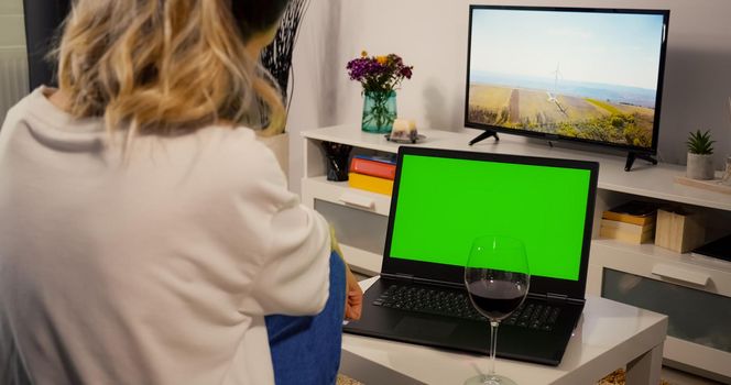 Over shoulder Laptop Green Screen for Copy Space Close up Chroma Key Mockup view. Happy woman has Video Call on with a Friend while Drinking a Glass of Wine. Video call Conversation Concept.