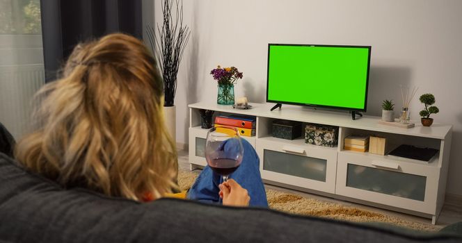 Woman Drink red Wine relaxing on a living room couch while watching tv Greenscreen and Chroma Key. Mock Up with Tracking Markers and Alpha Matte. Over the Shoulder view.