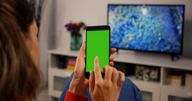 Woman Using Smartphone with Green Screen for Copy Space Chroma Key Mock Up with Tracking Markers and Alpha Matte. Touch Gesture. Watcing Gadget and make Touch on screen. Over the Shoulder view.