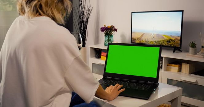 Woman make online shopping on laptop with Greenscreen and Chroma Key Mock Up with Tracking Markers and Alpha Matte. Female Using Laptop and Drink Wine in the Evening.