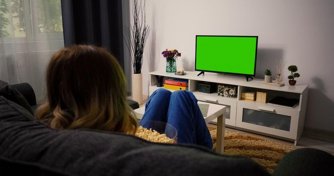 Woman Sitting on a Couch Home Watching Green Chroma Key Screen, Relaxing. Girl in a Cozy Room Watching Sports Match, News, Sitcom TV Show or a Movie on Green Screen eating popcorn.