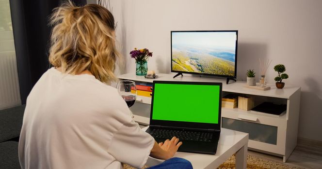 Woman sitting on sofa Using Laptop with Greenscreen and Chroma Key. Mock Up with Tracking Markers and Alpha Matte. Caucasian Female relaxing in the evening on laptop and drink wine. Web search.