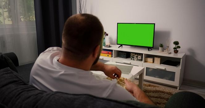 Man Watching Green Screen TV Chroma Key. Back View of a Middle Aged Man Sitting on a Couch Relaxing Living Room on Tv.