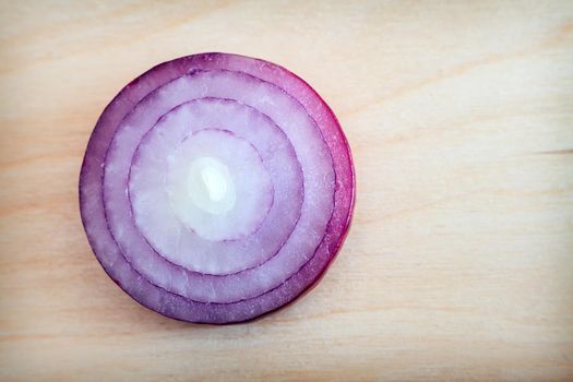 On a wooden background is a cross section of a blue onion bulb, top view. Healthy food concept, natural product.