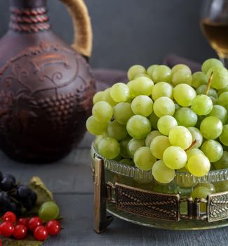 On the table in glass vase green grapes, near ceramic jug and two glasses guilt.