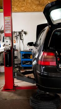 Car repair and maintenance in the auto repair small garage. Replacing car brake disc, pads. Car half body lifting for under repair isolated. vertical shot