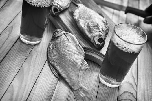 On a wooden table two glasses of beer, next to the cutting Board dried fish and a knife, black and white photo