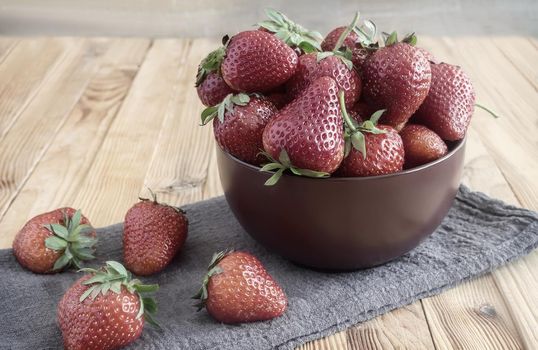 On the surface of the wooden table is a ceramic bowl of berries ripe strawberries. Presented close-up.
