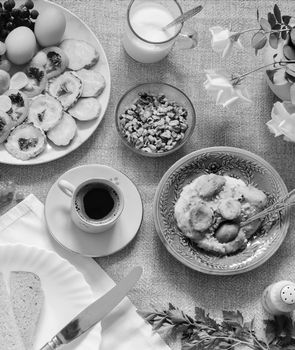 Healthy Breakfast: pumpkin puree with dried apricots, muesli, kefir, vegetables, eggs, coffee. Presented on a homespun rustic tablecloth, top view. Black and white image