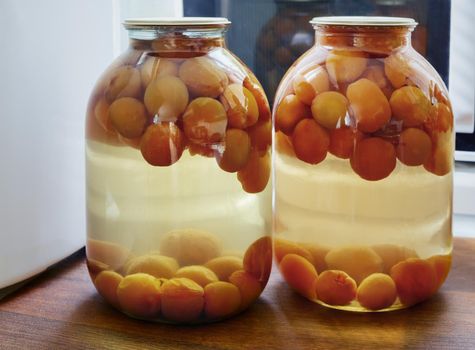 Home preservation of products: glass jars with compote of ripe apricots, hermetically sealed