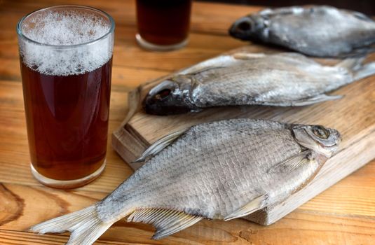 On a wooden table two glasses of beer, next to the cutting Board dried fish and a knife.