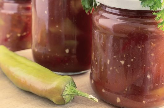 In glass jars Lecho of canned bell peppers and tomatoes, near fresh peppers and tomatoes