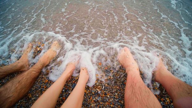 People standing with their feet in the sea water on the seashore. Summer and rest. Foot massage. Go barefoot at the sea beach. Beach with many shells.