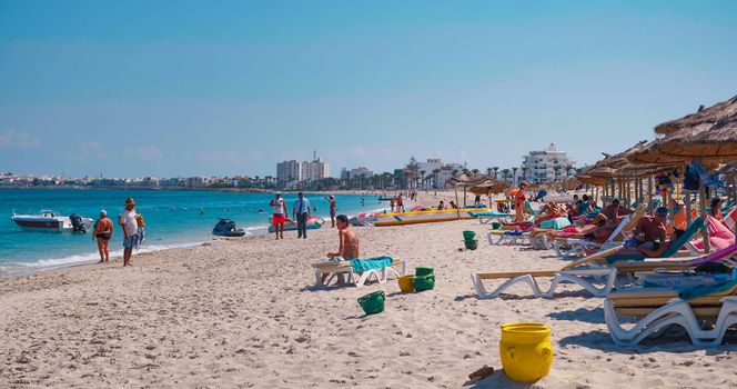 Tunisia, 2021: Crowded beach. People on the beach in vacation. People relaxing on a summer day under sun umbrellas. View of african seaside.