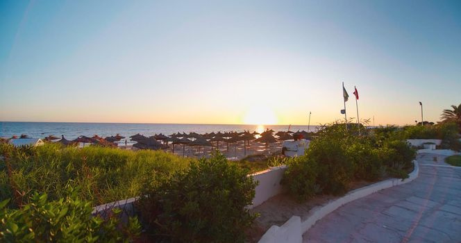 Beautiful beach resort at the sunset in Tunisia. Beach reed umbrellas, summer holidays.