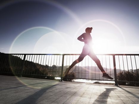 Side view silhouette of a runner man running on the beach bridge at sunset with sun in the background