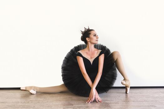 graceful ballerina in black swan dress against white background. Young ballet dancer practicing before performance in black tutu, classical dance studio, copy space