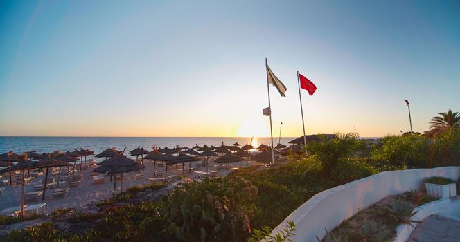 Luxury summer beach resort. Beach reed umbrella from Tunisia. Sea water on the sunset. Vacation and travel concept.