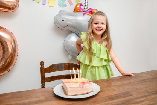 A girl and a pink cake with five candles for her birthday