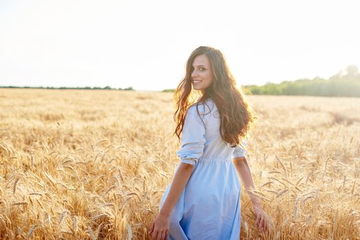 A young woman walks through a wheat field and looks at the camera