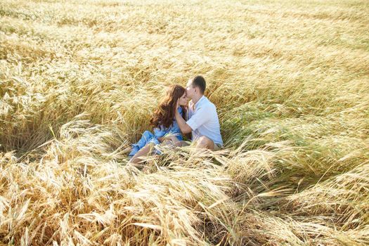 Lovely young couple kissing while sitting in a field. Love in the summer.
