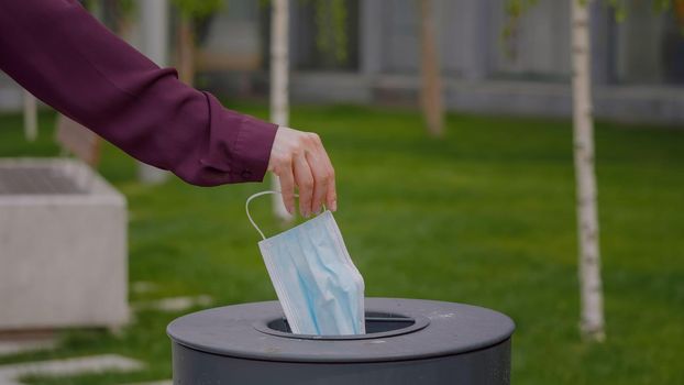 Woman throws a medical mask into the trash outdoors Used face mask is dumped in a trash. Medical protective mask using to health protection from corona virus.