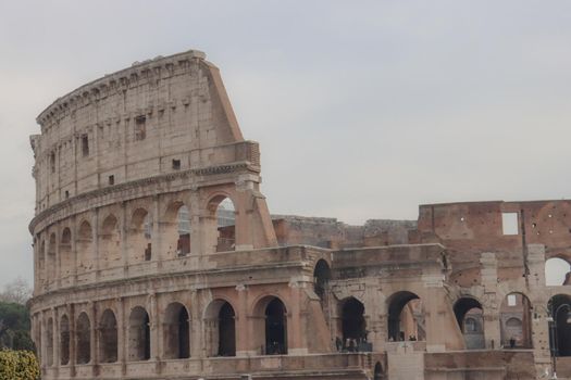 ROME, ITALY - February 05, 2022: Panoramic view around the Colosseum in city of Rome, Italy. Cold and gray sky in the background. Macro photography of the green parks with the old buildings.