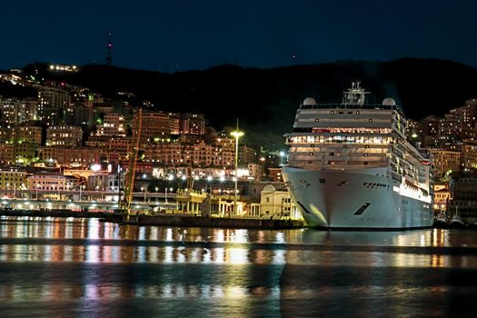 Genova, Italy - July 02, 2022: View of the city and the old harbor (Porto Antico) by night. City lights reflection over the water.