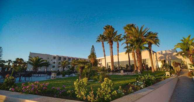 View of hotel with tropical garden, palm trees. Vacation destination in Tunisia. Beautiful resort on the Mediterranean Sea beach.