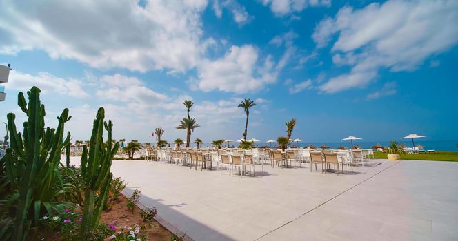 Tunisia, 2022: View of luxury terrace on a tropical beach in Tunisia, Africa. Beautiful garden on a luxury hotel, palm trees on seaside. Resort overlooking the Mediterranean Sea.