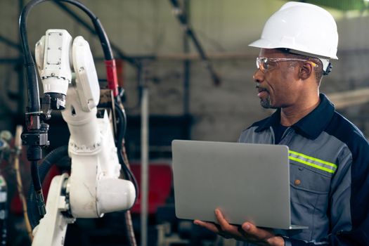 African American factory worker working with adept robotic arm in a workshop . Industry robot programming software for automated manufacturing technology .