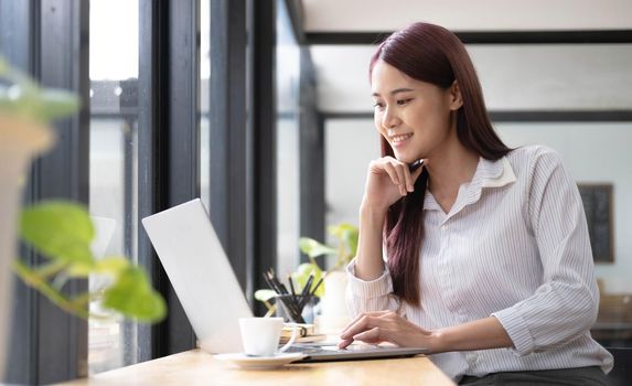 Close up portrait of a beautiful young Asia woman smiling and looking at laptop screen.