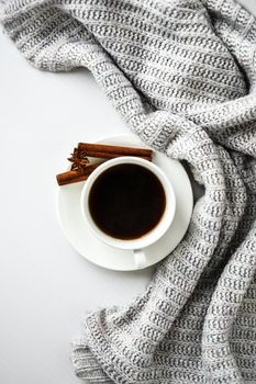 Cup of coffee with cinnamon sticks and anise star on white background. Sweater around. Winter morning routine. Coffee break. Copy space. Top view. Breakfast. Flat lay