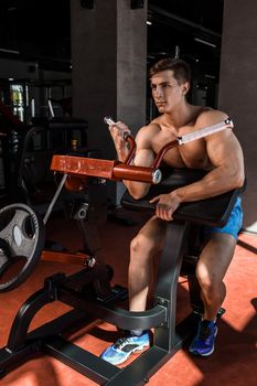 Tense muscles of hands under load. Man doing exercise for biceps in the gym. Work on tell muscles on the simulator. Photos for sporting magazines, posters and websites.