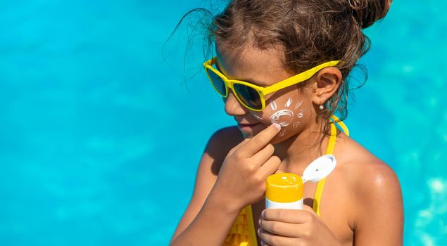 Sunscreen near the pool on the face of the child. Selective focus. Kid.